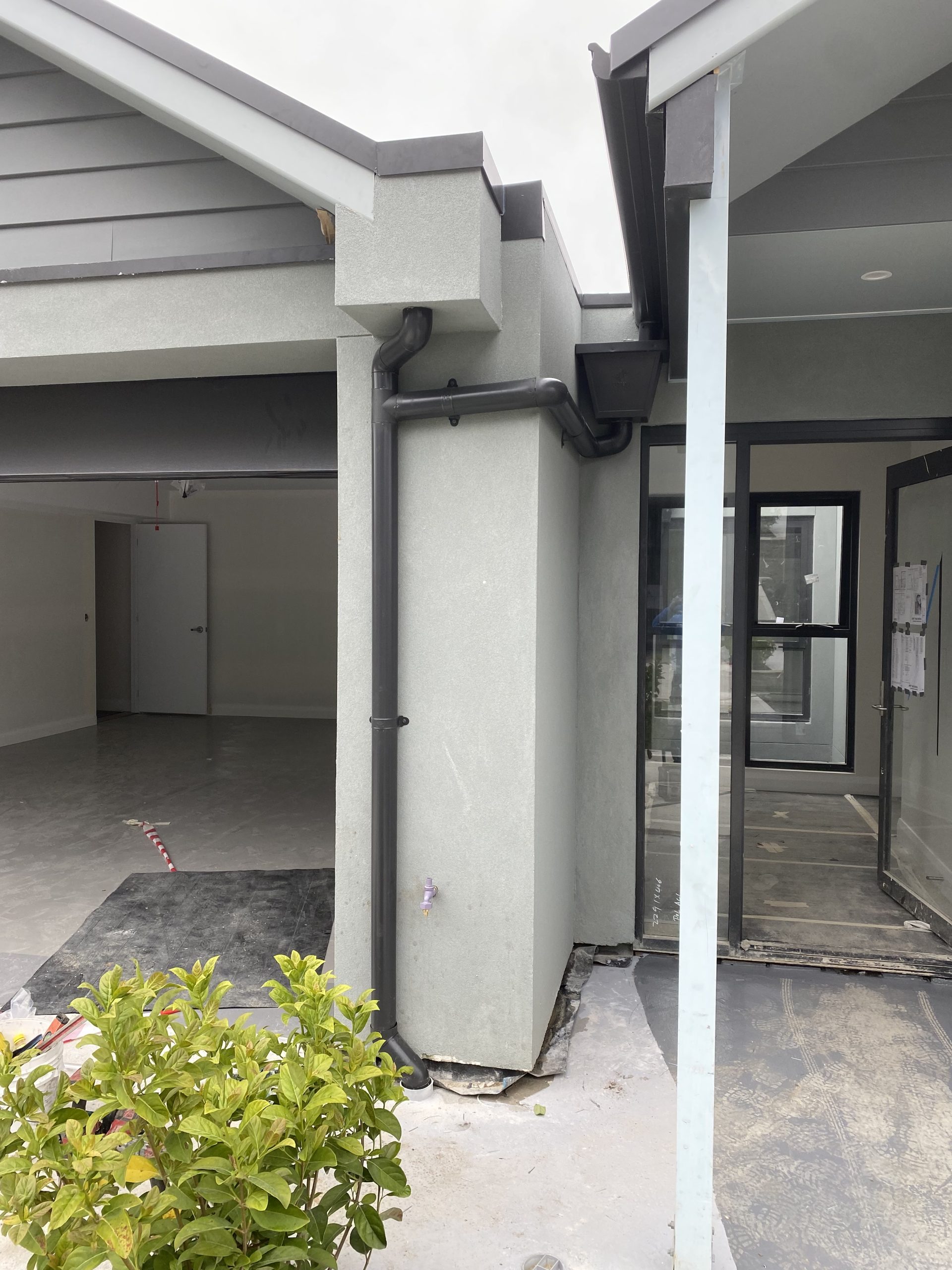 Exterior corner of a building under construction, showing black gutters and a downpipe on a light gray stucco wall